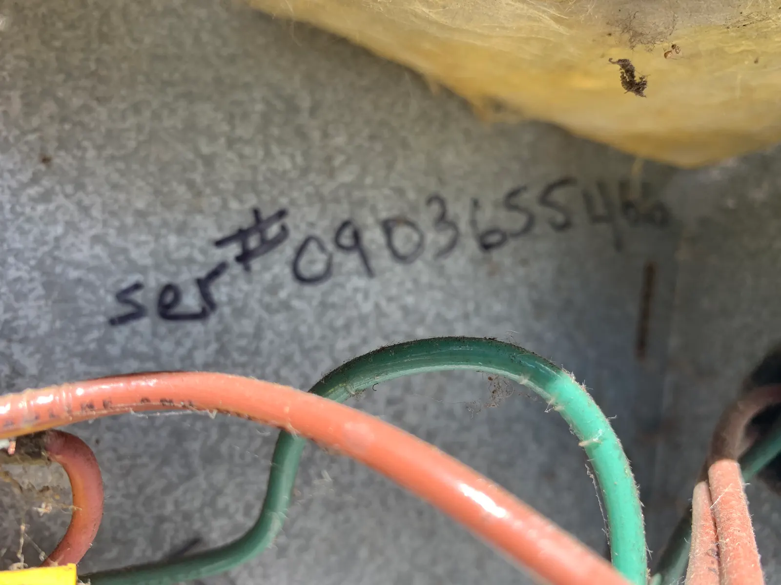 Handwritten serial number on the metal housing of an aging air conditioning unit